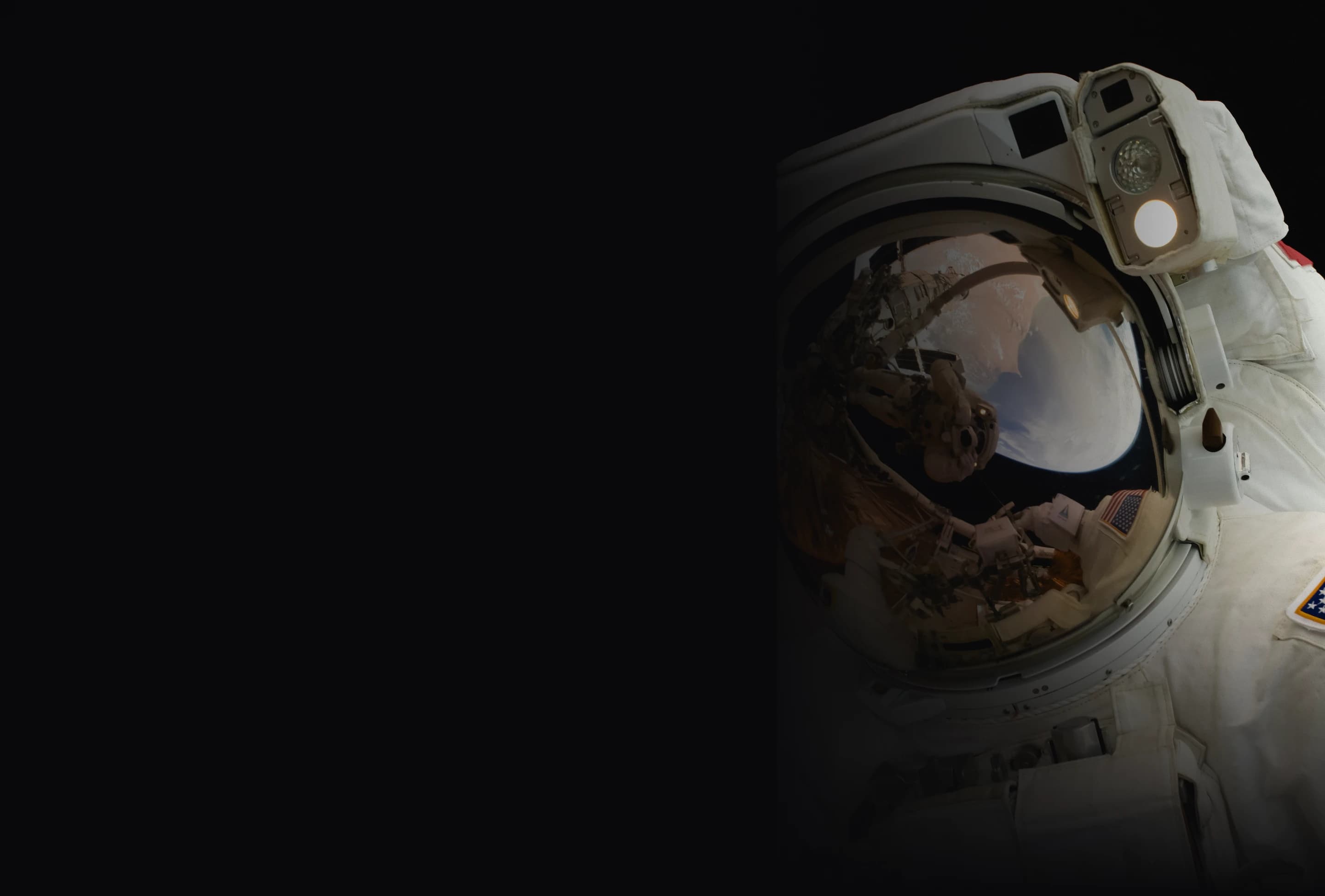 Close-up of an astronaut’s helmet during a spacewalk, with the reflection showing Earth and parts of the spacecraft.