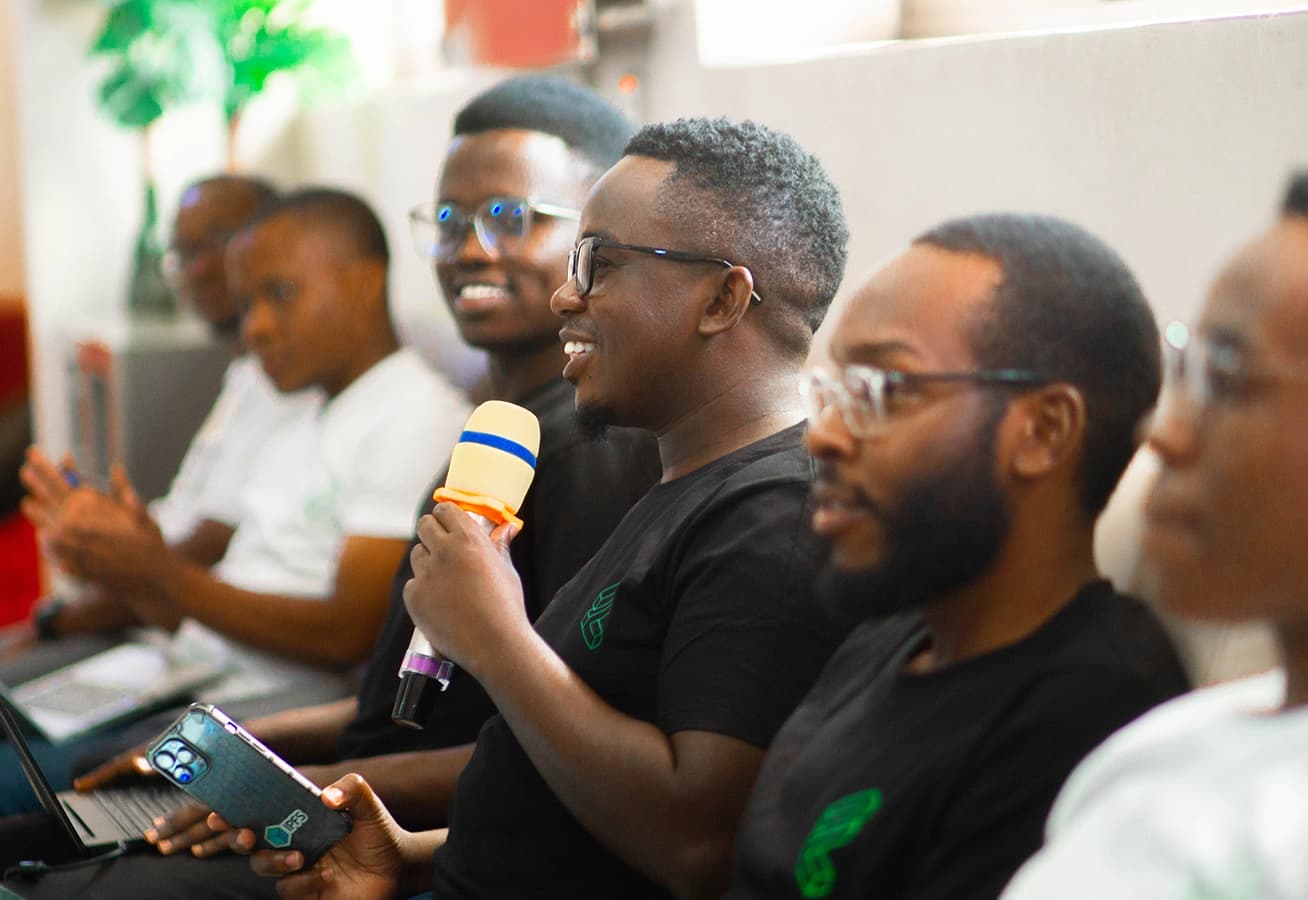 A man speaks into a microphone during a discussion panel, smiling while other participants listen attentively beside him.