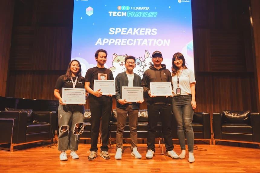 Five speakers standing on stage holding certificates of appreciation during a tech conference, with a “Speakers Appreciation” sign projected behind them.